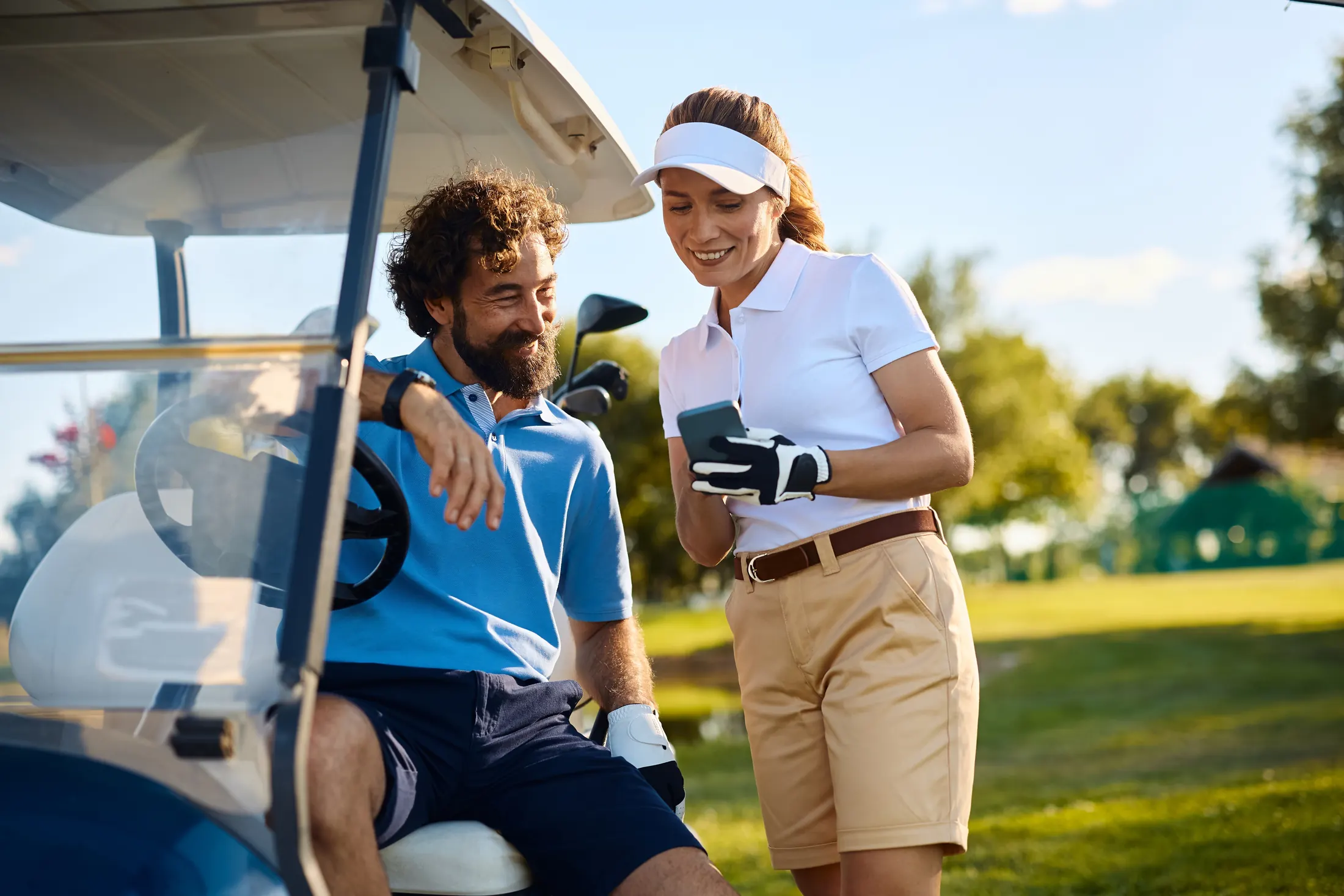 Two golfers at a buggy looking together at a phone screen between shots